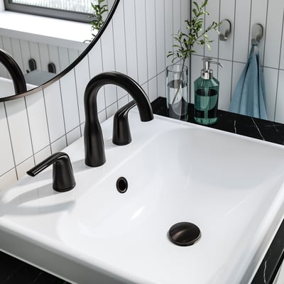 Modern bathroom sink with black tap, drain, and soap dispenser. Clean, minimal design with white ceramic basin. Reflects in round mirror.