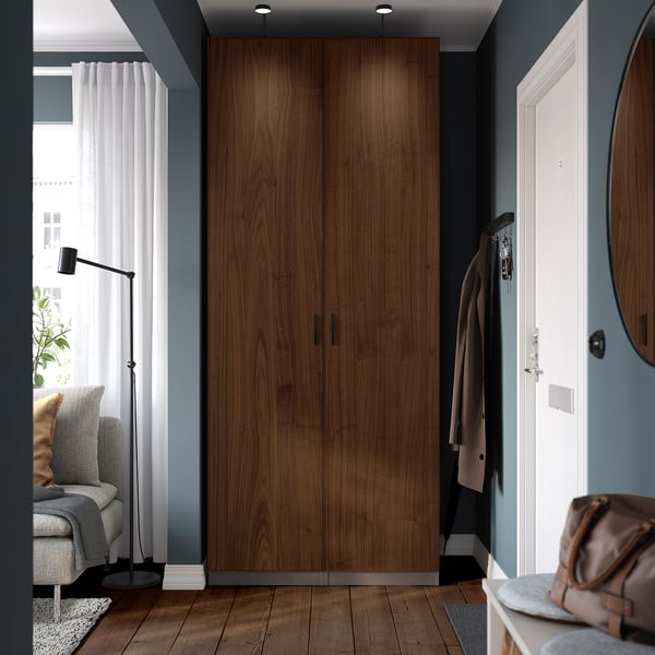PAX wardrobe: tall wooden closet, wall-spanning, divides room, houses clothes, near couch & lamp.