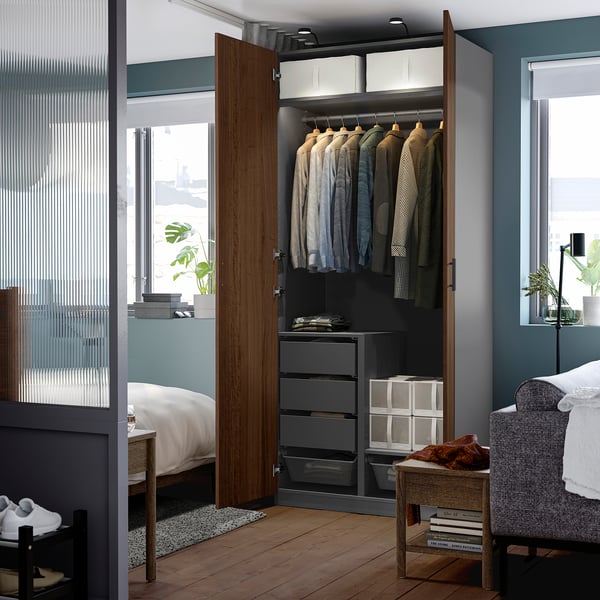 Open wardrobe displaying shirts, drawers, and shelves. Room includes bed, armchair, and window.