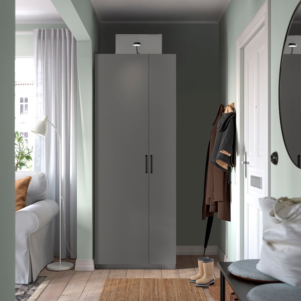 Modern entryway with grey PAX wardrobe, white door, grey sofa, coats, and boots.