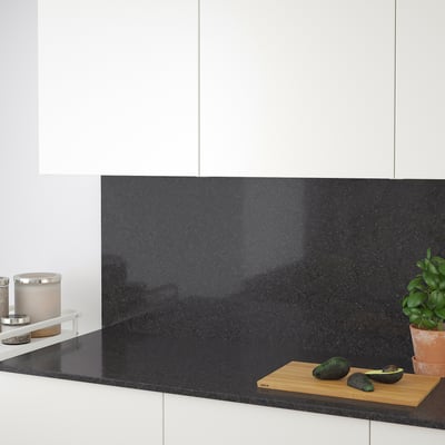 Modern kitchen countertop shows avocados on cutting board. Dark quartz surface, white cabinets.