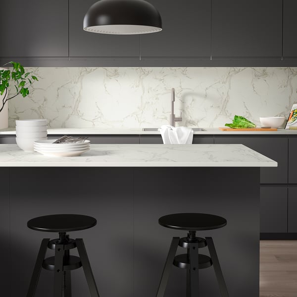 Modern kitchen with grey cabinets, white marble countertop, black stools, and pendant light.