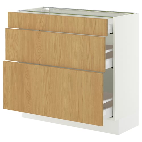 A modern, white kitchen cabinet with light wood drawers. It three drawers and an open shelf. The design is sleek and functional.