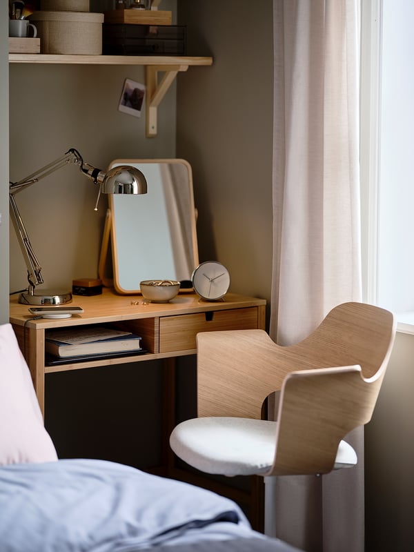 Modern bedroom with wooden desk, chair, lamp, and mirror. White curtains by window, blue bedding visible.