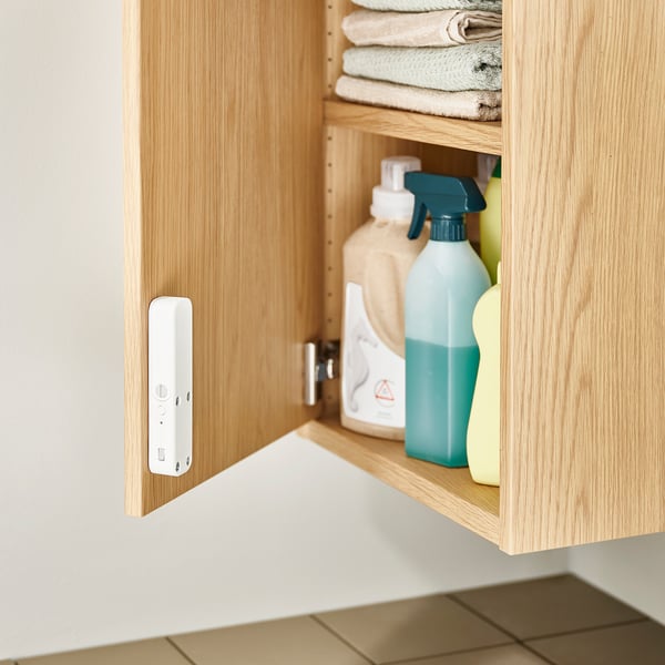 An open wooden cabinet with cleaning supplies inside, including a white lock on the door.