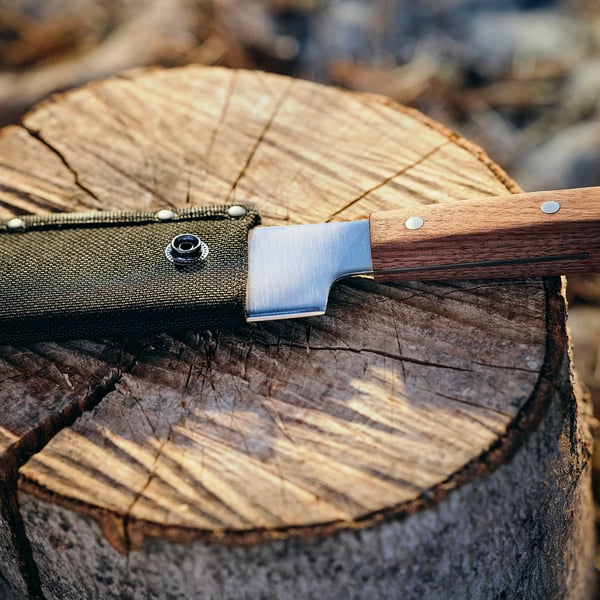 A knife on a wooden stump. It has a wooden handle and a metal blade. Used for chopping.