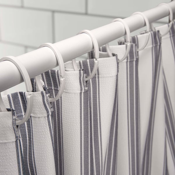 White shower curtain with grey stripes hanging on a metal rod using plastic hooks.