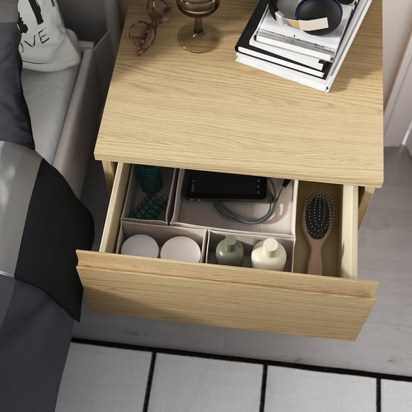 Wooden bedside table with drawer, toiletries, brush, chair, and accessories.