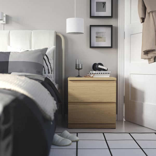 Minimalist bedroom with STORKLINTA wooden bedside table. Lamp, books, headphones. Grey bed linens.