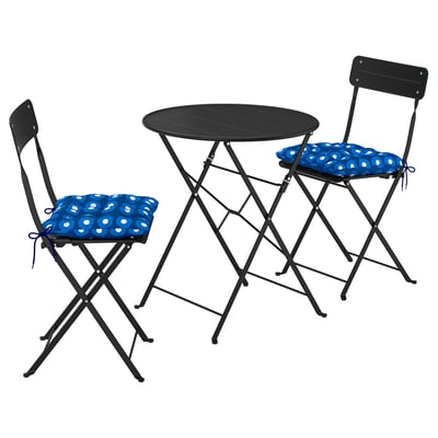 A black SUNDSÖ outdoor bistro set with a round table and two foldable chairs, each adorned with blue and white polka dot cushions.