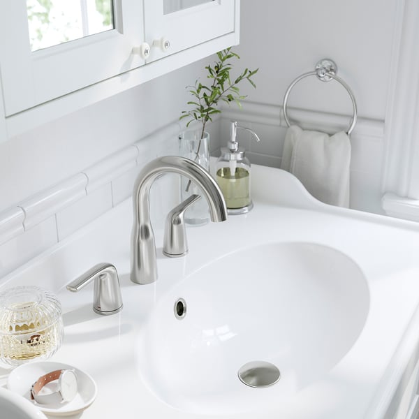 A modern bathroom sink with chrome tap, green soap dispenser, and small plant on a white countertop beside a mirror.