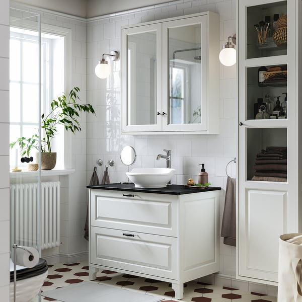 Modern white bathroom vanity, TÄNNFORSEN, with sleek drawers, vessel sink, glass cabinets, mirrors, and wall lights. Geometric tile floor.