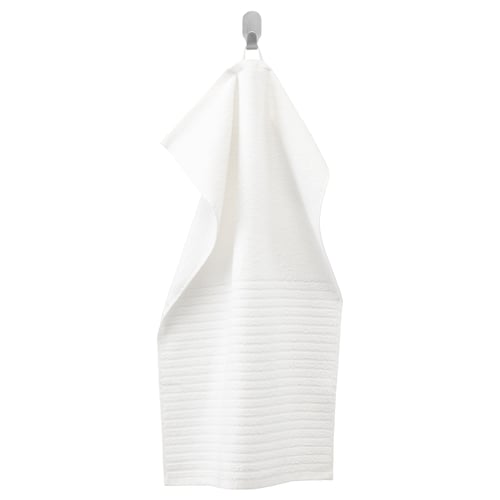 The VÅGSJÖN white cotton towel hangs neatly on a hanger. Its texture combines solid terry and striped patterns, providing softness and absorbency.