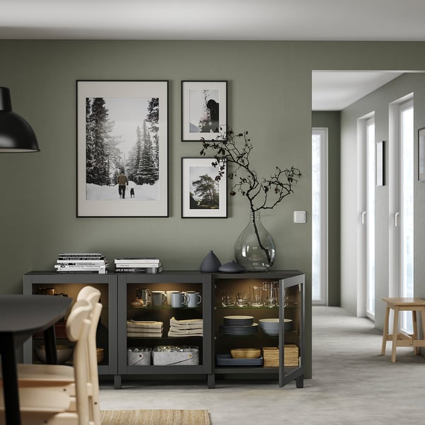 Modern dining room with green walls, grey cabinet, black light, vase, photos, books, plates, cups, wooden chairs.