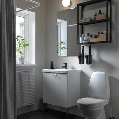Minimalist bathroom: ENHET cabinet, sink, toilet, mirror, shelves. Matte black tap, grey curtains, dark floor, plant.