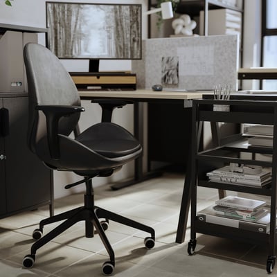Modern office desk setup with ergonomic black chair, computer, and bookshelf.