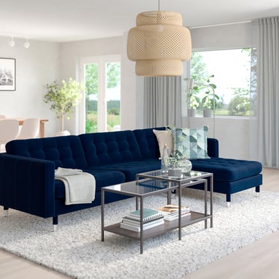 Modern living room: dark blue l-shape sofa with metal coffee table, plants, and large window.