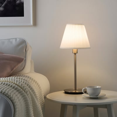 Small, white MYRHULT lamp sits on side table beside armchair, casting soft light.