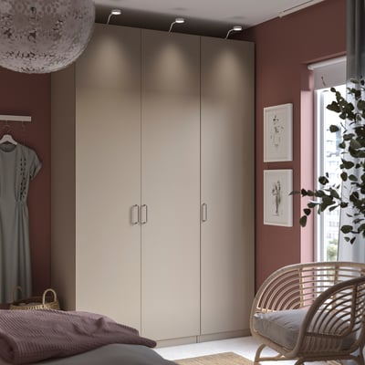 Modern bedroom with beige PAX wardrobe, wicker chair, grey bedding, and red walls.