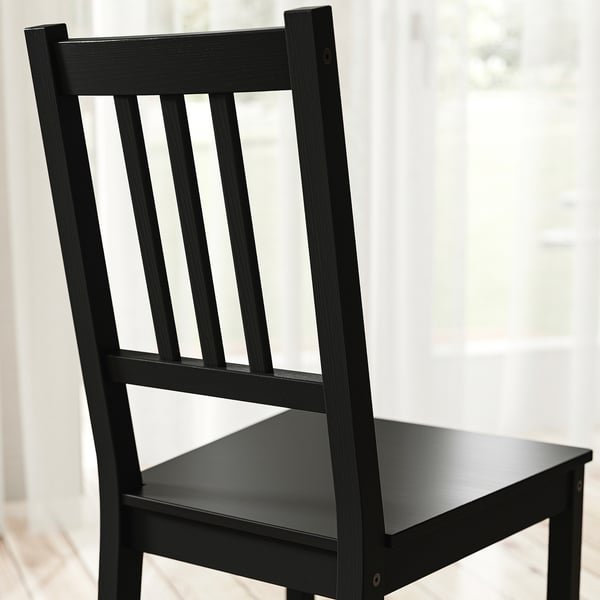 Black wooden chair with vertical slatted back and seat, sturdy and well-finished, standing against a bright window.