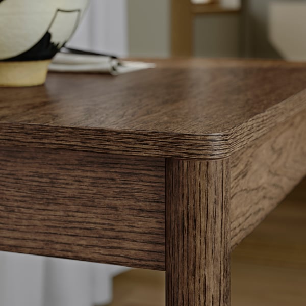 Wooden table with visible grain patterns. The edge and corner joints are well-crafted. Smooth, polished surface reflecting light.