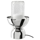 ACKJA lamp: modern metal bowl base, clear hammered glass bulb, nickel finish, emits warm glow.