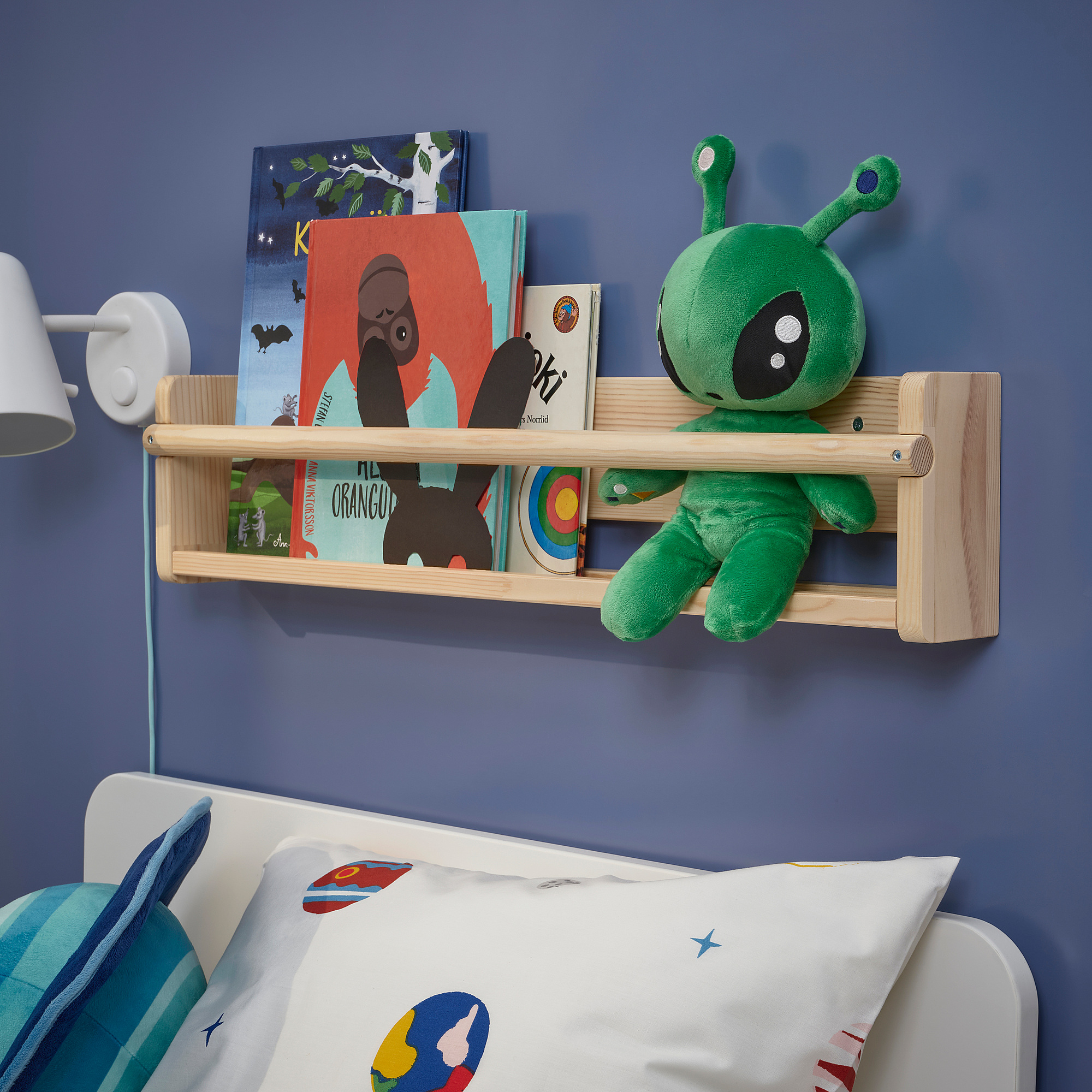 Blue wall with books, alien toy, bed with colorful pillows.