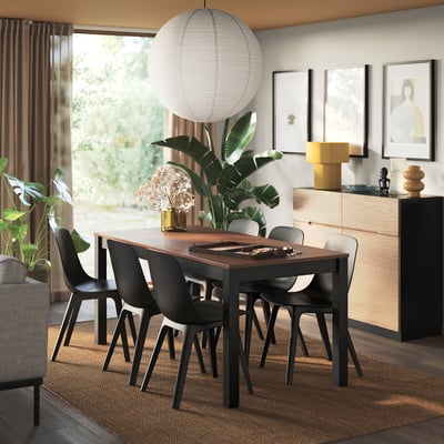 Modern dark wood dining table, ÅLHULT, seats six, well-lit room with plants.