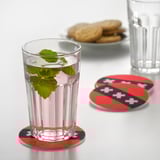 Glass of water on red coaster resembling amsterdam flag, initials ams in white. Two more coasters and cookies in background.