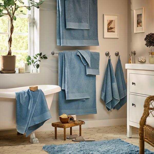 Bathroom with blue mats, towels, plants, white fixtures.