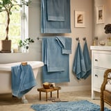 Bathroom with blue mats, towels, plants, white fixtures.