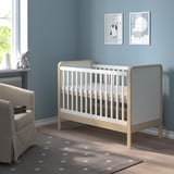 Beige cot against blue wall, grey rug, near armchair.