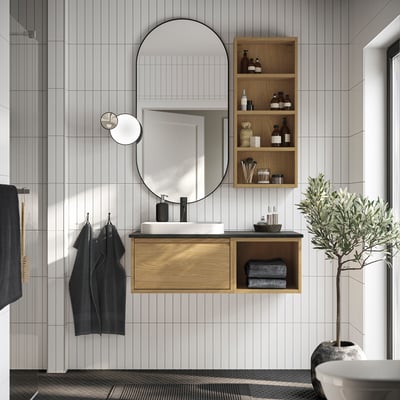 Modern bathroom with white & wood cabinet, round mirror. Plant & towels add cosiness. Sink is marble.