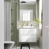 Modern white vanity with sink, mirror cabinet, stool, and striped shower curtain.