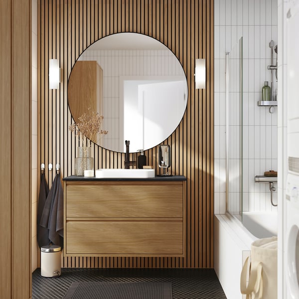 Modern bathroom with ÄNGSJÖN oak sink, large mirror, cabinet, and gold-fixture bathtub.