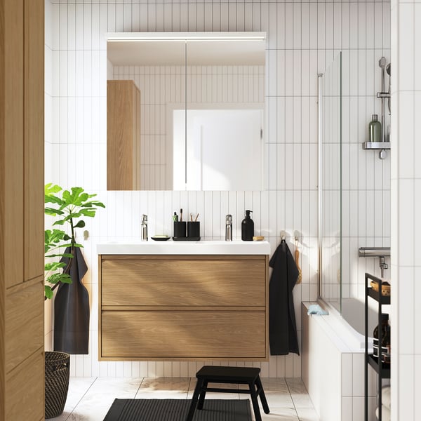 Oak bathroom vanity with drawers and double basin, wall-mounted, mirror cabinet, black accents, plant.