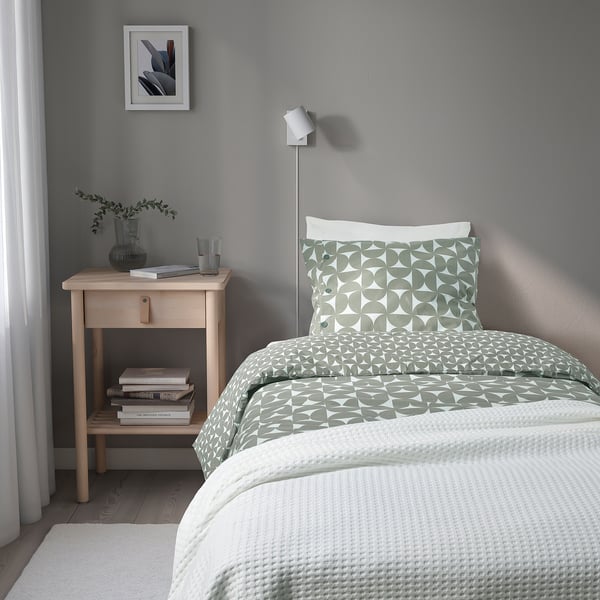 Modern bedside table with geometric duvet, books, and wall lamp. Alternative: bedside table with pattern duvet, books, and wall lamp.