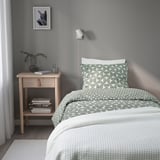 Modern bedside table with geometric duvet, books, and wall lamp. Alternative: bedside table with pattern duvet, books, and wall lamp.