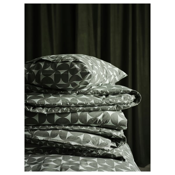 Folded green bedding set with circular patterns, including duvet cover and pillowcases, resting against dark curtains.