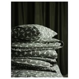 Folded green bedding set with circular patterns, including duvet cover and pillowcases, resting against dark curtains.