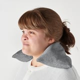 A woman hold a microwavable heating pad on her shoulder for neck and shoulder relief.