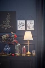 Dark room with blue walls; black cabinet holds brass lamp, vases, and decorative pieces; artwork above.