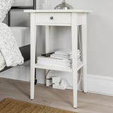 Small white nightstand with open shelf, books, phone, and adaptive power. ÅSKVÄDER series, bedsid.