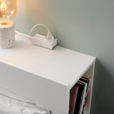 An a white surface with an ÅSKVÄDER power module featuring an on/off switch and a bookshelf containing books, against a light green wall.