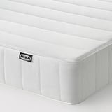 A close-up of a white mattress with horizontal lines, the IKEA logo visibly attached, showcasing its smooth, clean surface.
