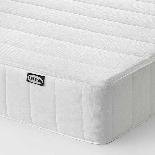 Shows a firm, white mattress by ikea, neatly cornered and pristine.
