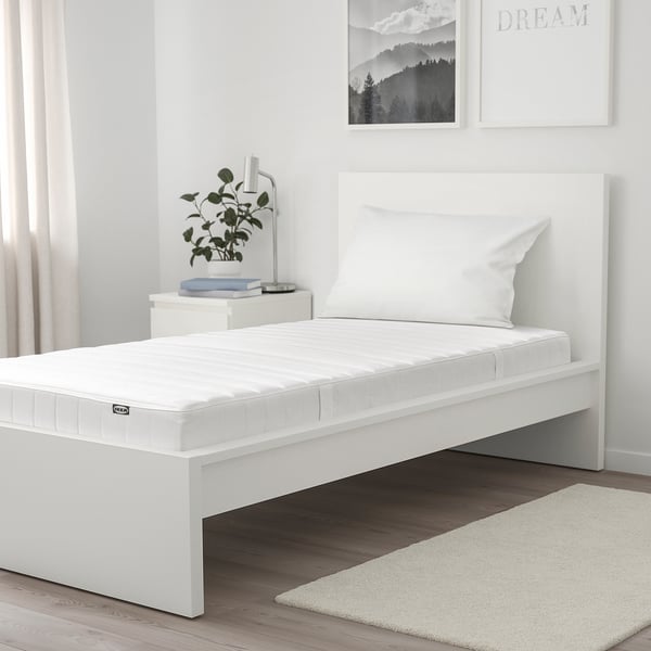 Modern white bedroom with ASPSJÖKULLEN mattress on low frame, decorated minimalist with plants, books, and wall art.