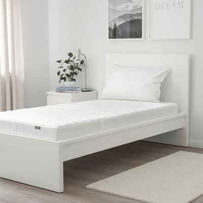 Modern white bedroom with ASPSJÖKULLEN mattress on low frame, decorated minimalist with plants, books, and wall art.