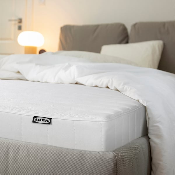 Neatly made bed with a white IKEA mattress, soft pillows, and a cozy, light-filled room.