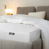 Neatly made bed with a white IKEA mattress, soft pillows, and a cozy, light-filled room.